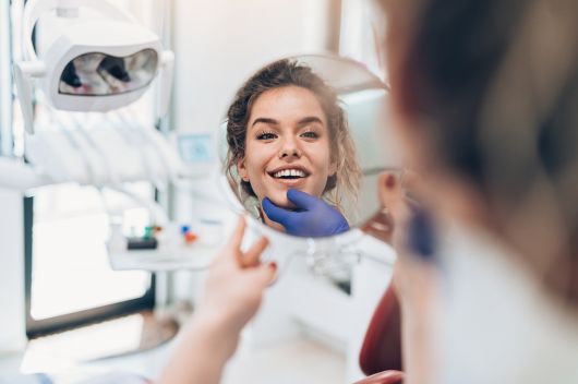 woman smiling into a hand held mirror